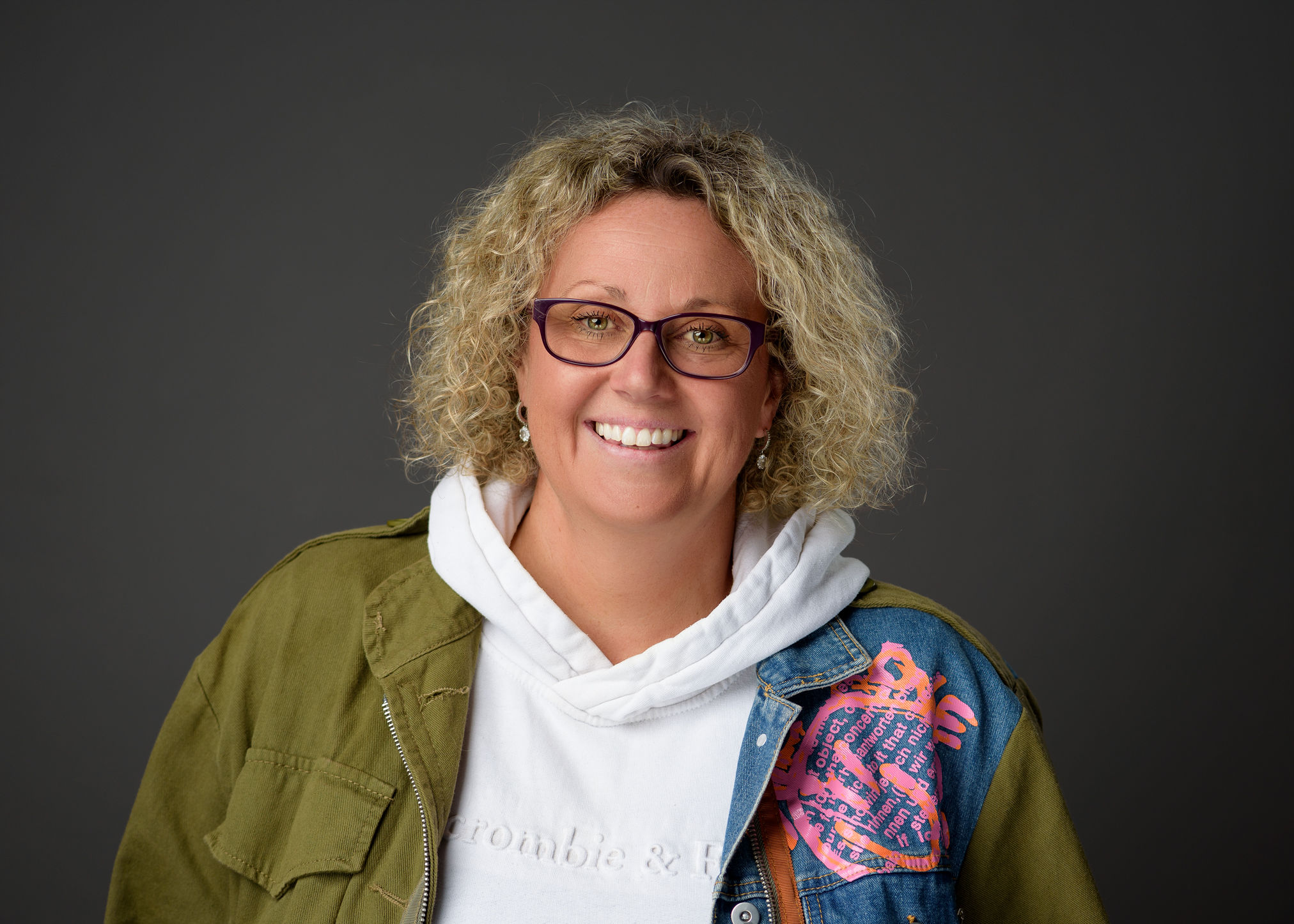 Anna Bates smiling, wearing glasses and a green jacket.