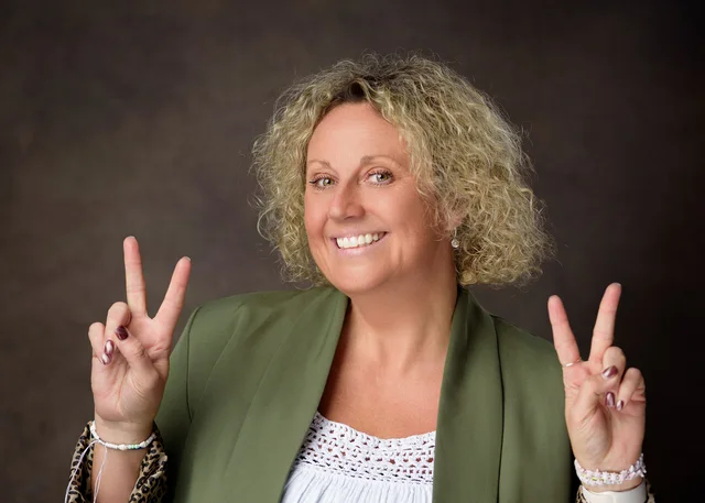 Anna Bates smiling and making peace signs with both hands in a green blazer.