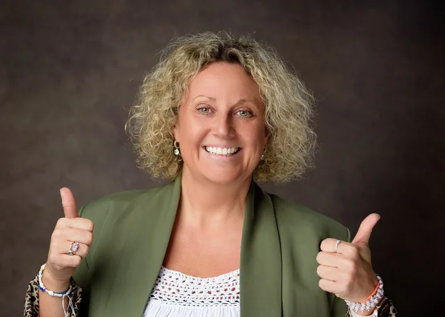 Anna Bates smiling and giving two thumbs up in a green blazer.